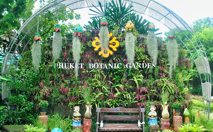 Phuket Botanic Garden entrance with lush greenery and decorative statues.