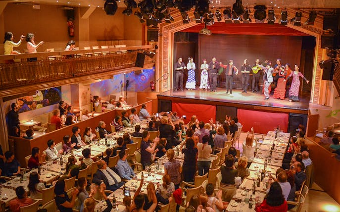 Flamenco dancers performing on stage with audience dining in a theater setting.