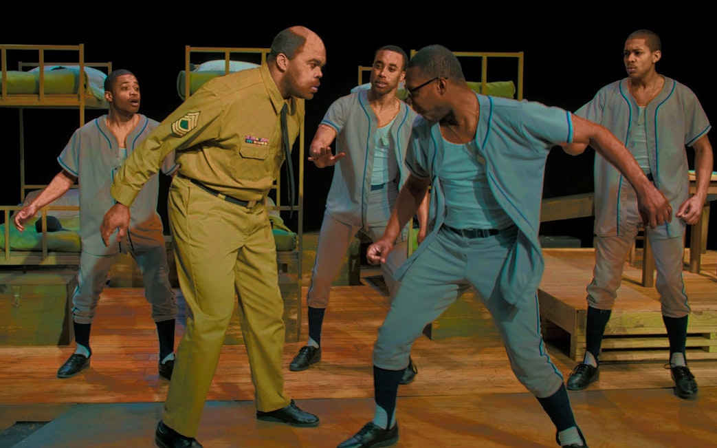 Actors performing a scene from "A Soldier's Play" on stage with bunk beds in the background.