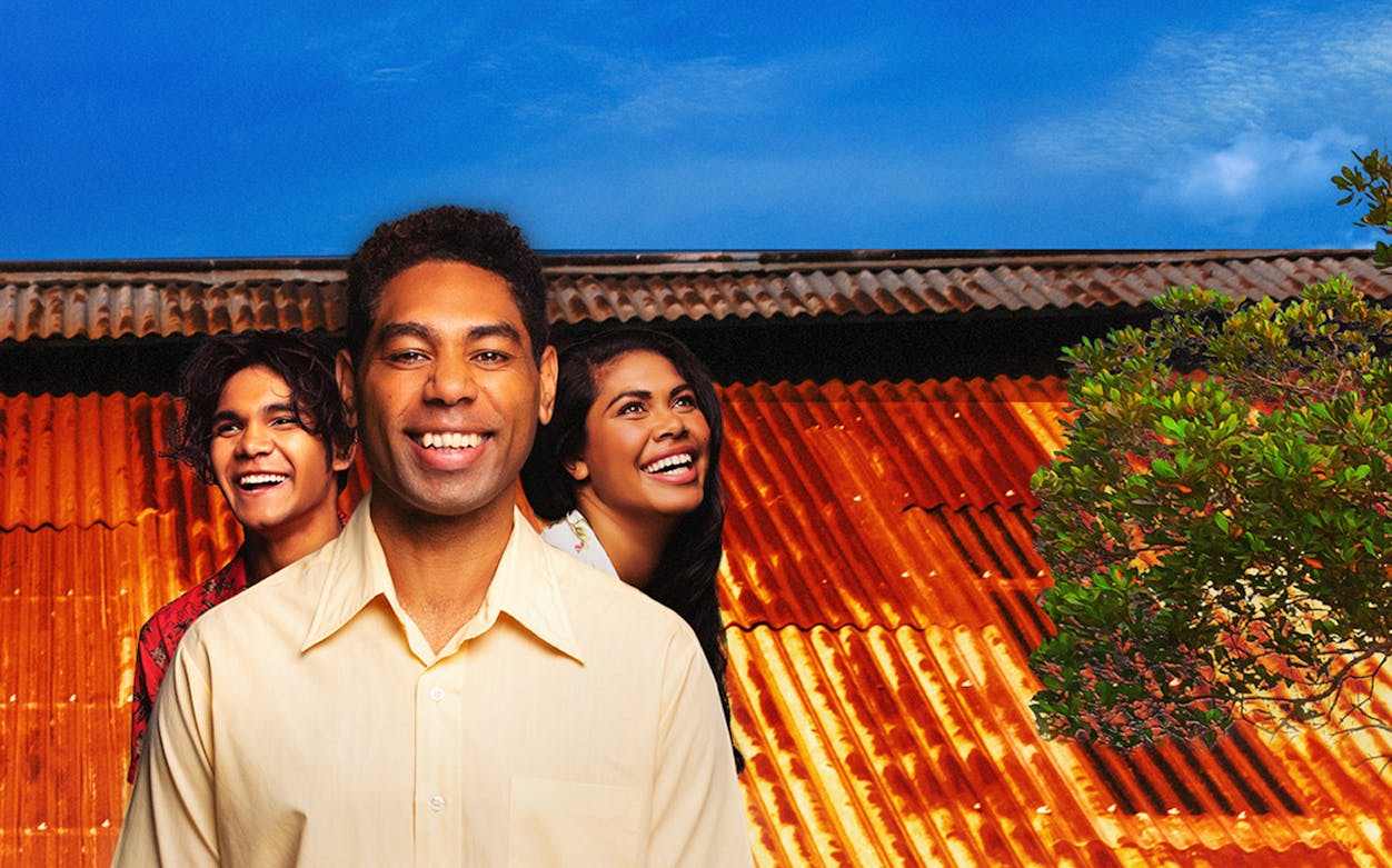 Three people smiling in front of a corrugated iron roof, related to Bran Nue Dae.