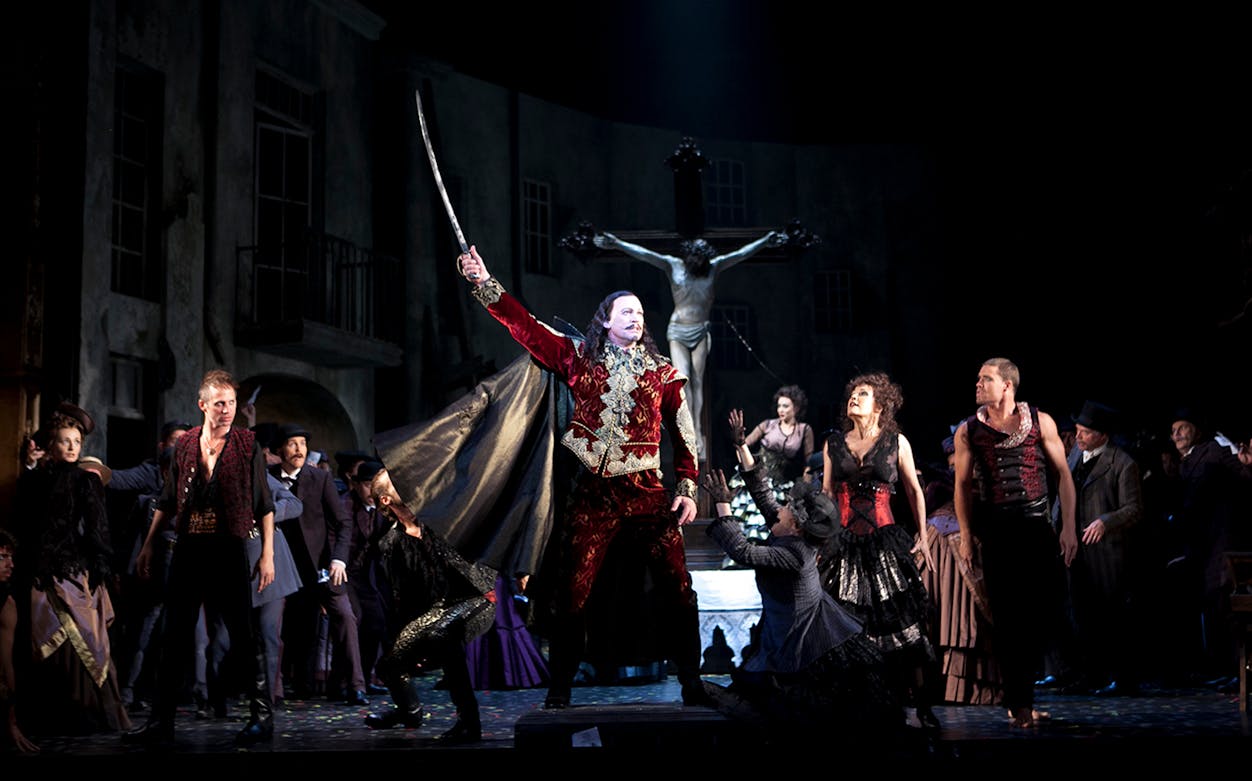 Stage performance of Faust with actors in period costumes, dramatic lighting, and a crucifix backdrop.