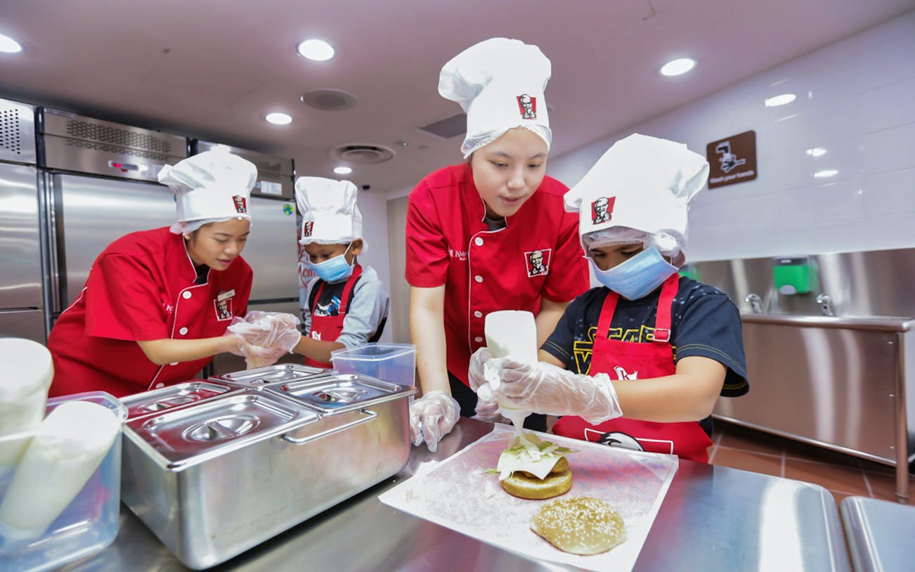 Children in chef hats making burgers at KidZania kitchen experience.