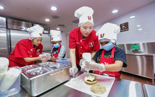 Children in chef hats making burgers at KidZania kitchen experience.
