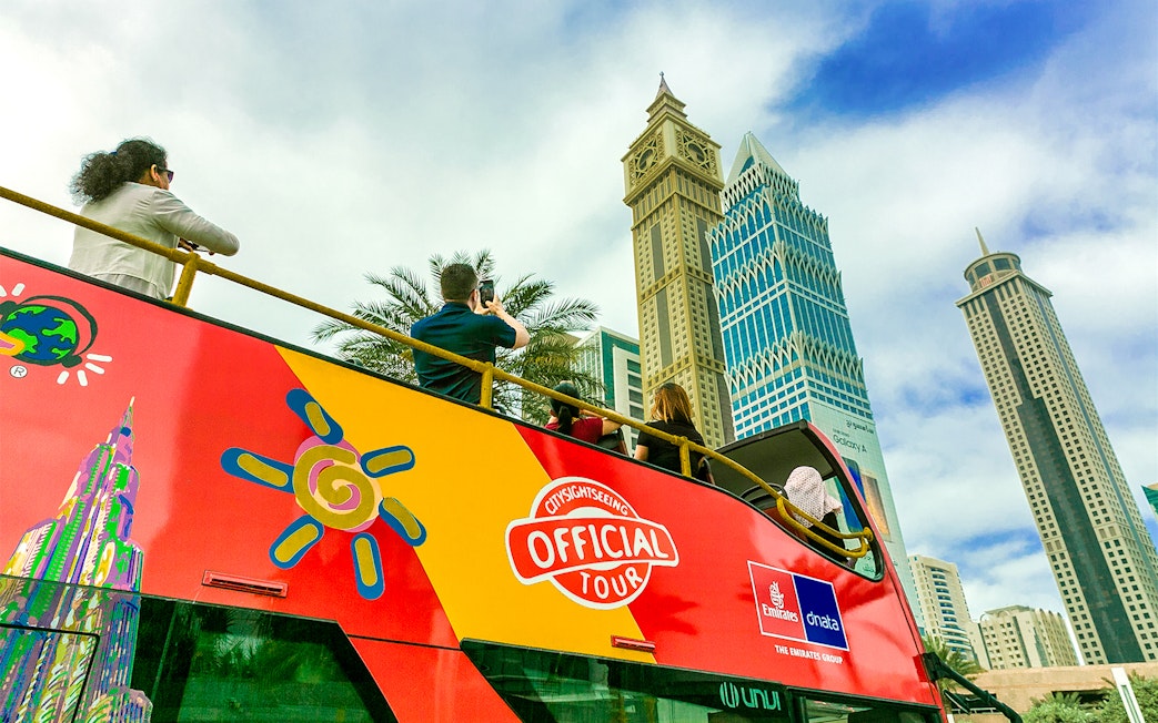 Open-top tour bus with tourists viewing Dubai skyscrapers.