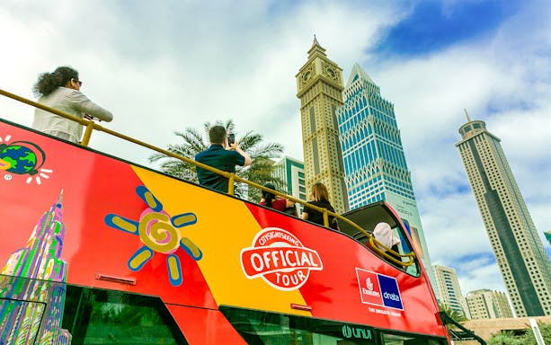 Open-top tour bus with tourists viewing Dubai skyscrapers.