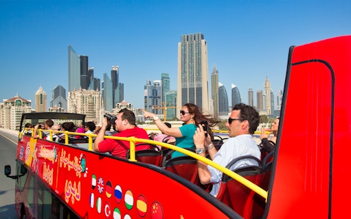 Open-top tour bus with tourists viewing Dubai skyline.