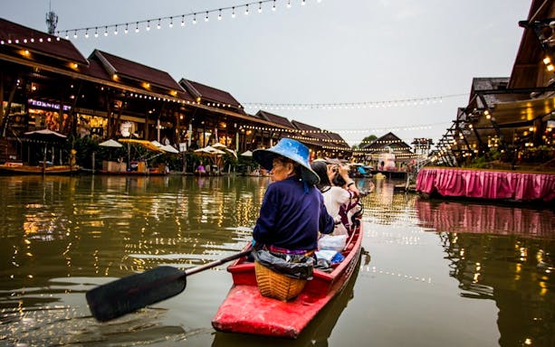 Visitors in a boat at Pattaya Floating Market, Thailand, surrounded by lit-up wooden shops.