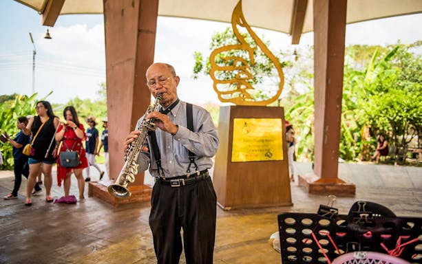 Musician playing saxophone at Pattaya Floating Market with sculpture in background.