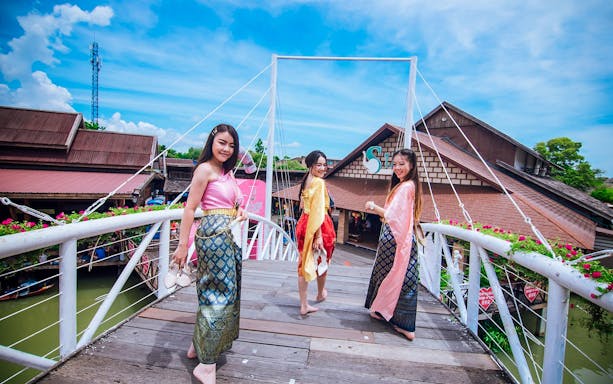 Women in traditional attire on a bridge at Pattaya Floating Market, Thailand.