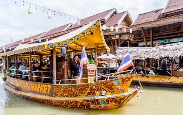 Boat with tourists at Pattaya Floating Market, Thailand, with traditional wooden buildings in the background.