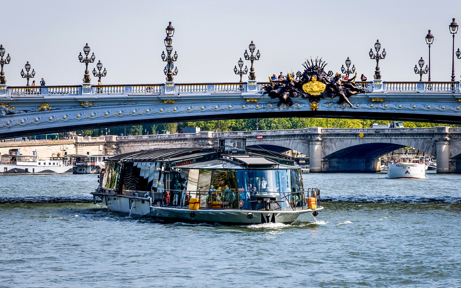 Seine River cruise passing from under a bridge on Seine River with tourists overlooking scenic views.