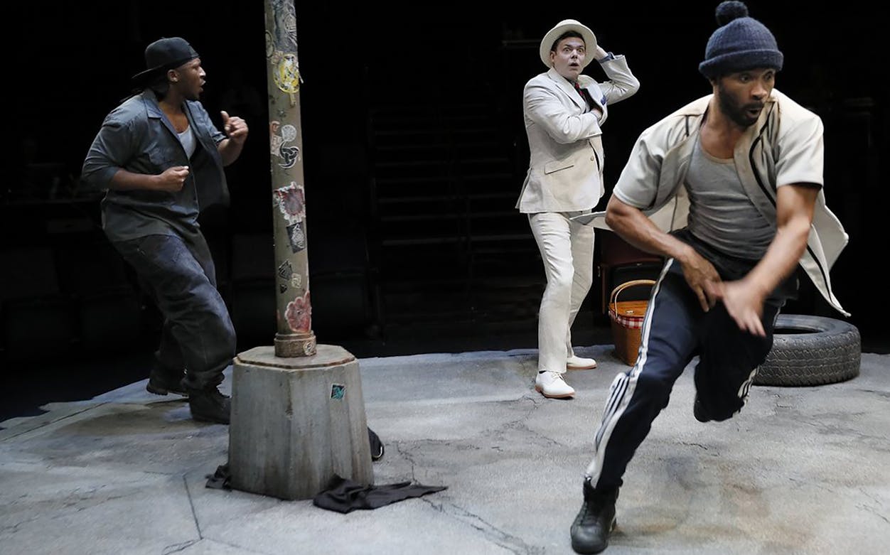 Three actors perform a scene from "Pass Over" on stage, featuring dynamic movement and expressive gestures.