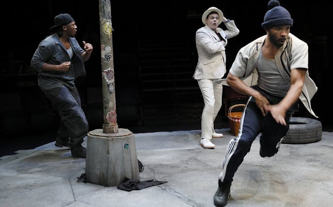Three actors perform a scene from "Pass Over" on stage, featuring dynamic movement and expressive gestures.