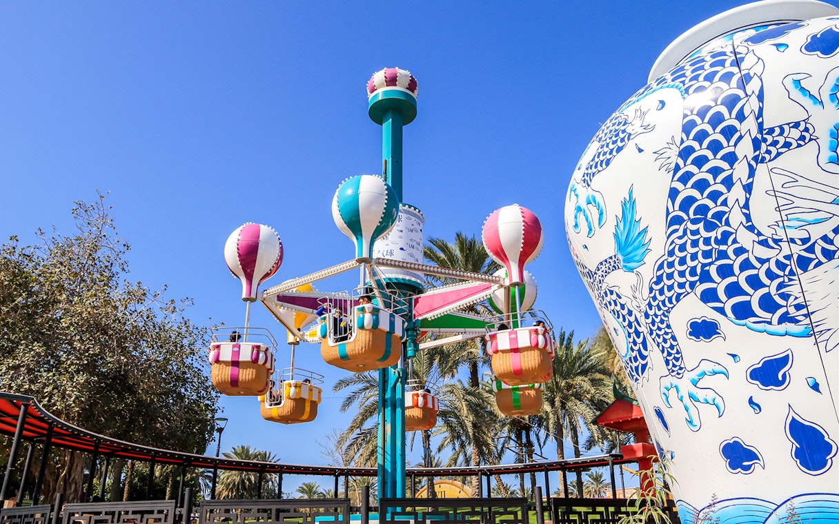 Colorful hot air balloon ride at Al Montazah Water Park, surrounded by palm trees and a large decorative vase.