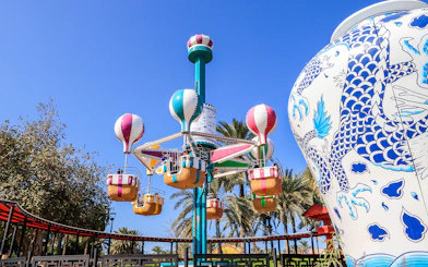 Colorful hot air balloon ride at Al Montazah Water Park, surrounded by palm trees and a large decorative vase.