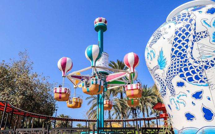 Colorful hot air balloon ride at Al Montazah Water Park, surrounded by palm trees and a large decorative vase.