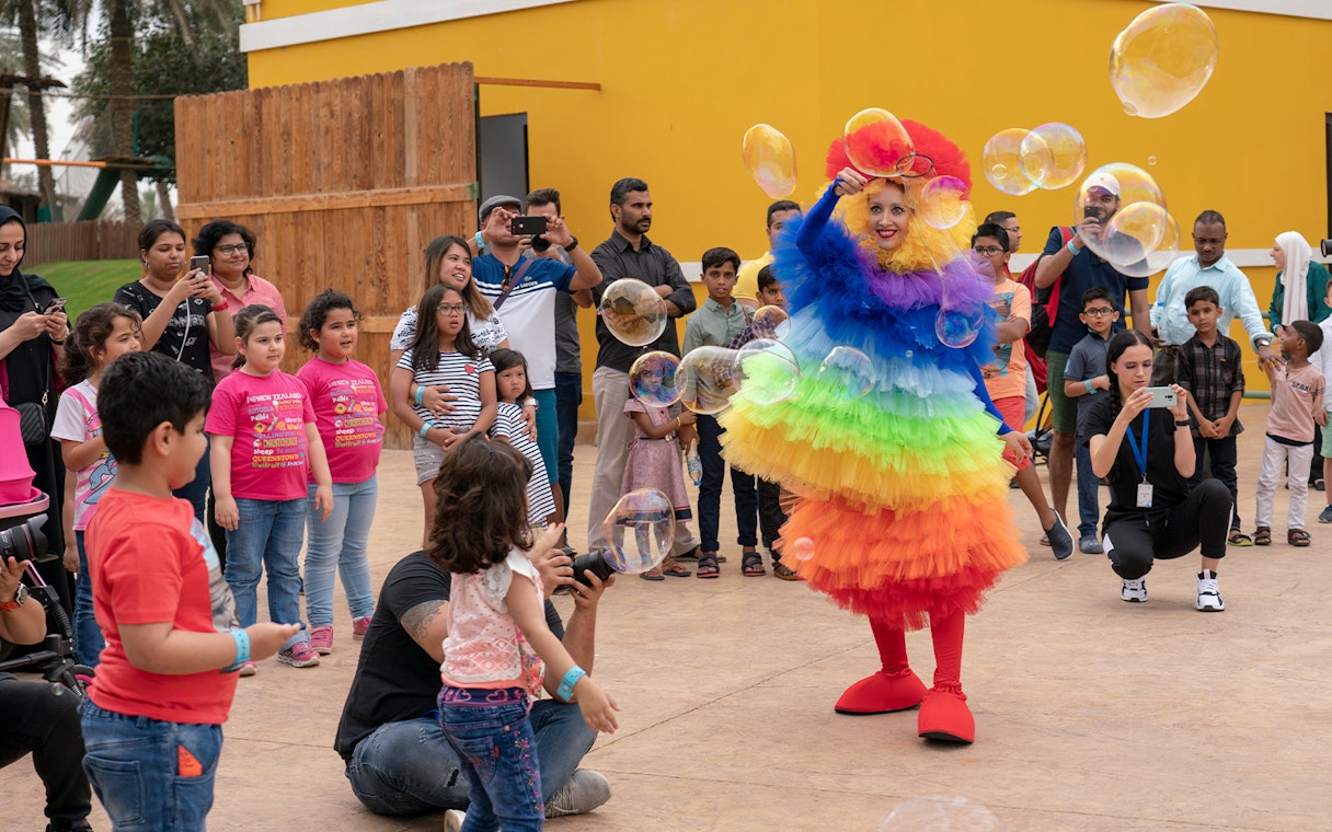 Performer in colorful costume entertaining children with bubbles at Al Montazah Water Park.