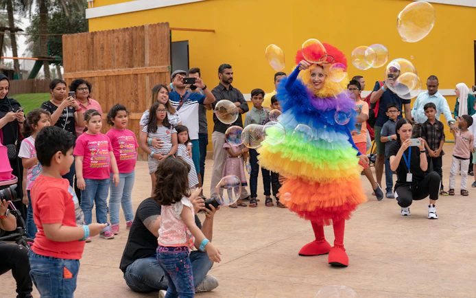 Performer in colorful costume entertaining children with bubbles at Al Montazah Water Park.