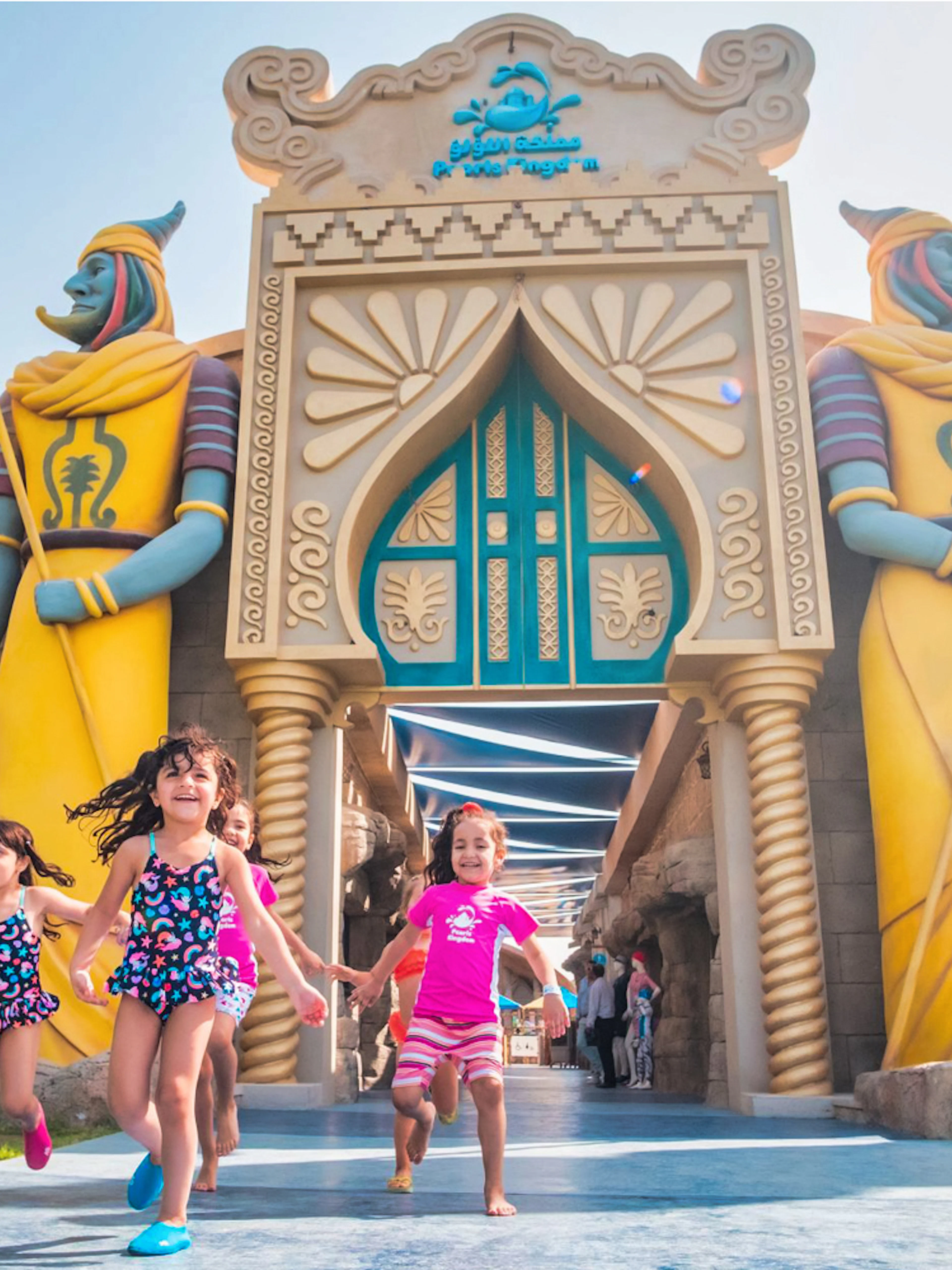 Children running at the entrance of Al Montazah Water Park with colorful statues.
