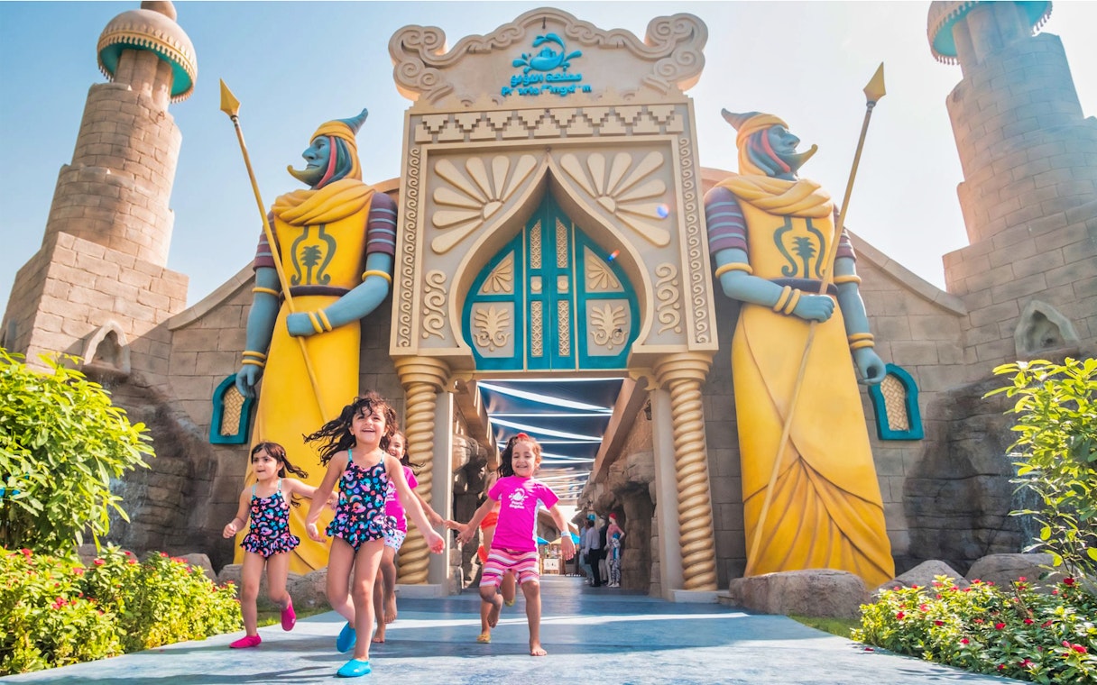 Children running at the entrance of Al Montazah Water Park with colorful statues.