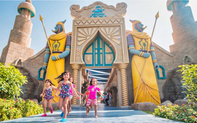 Children running at the entrance of Al Montazah Water Park with colorful statues.