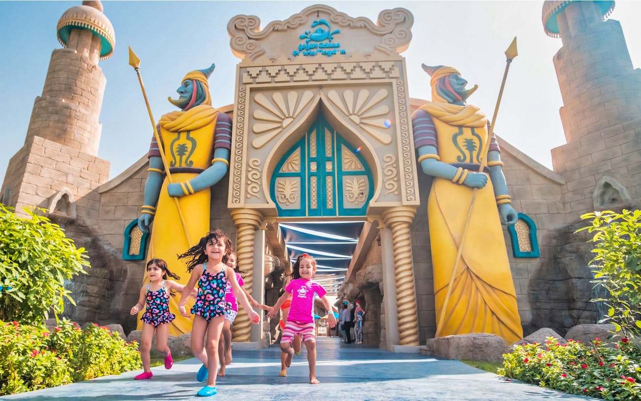 Children running at the entrance of Al Montazah Water Park with colorful statues.