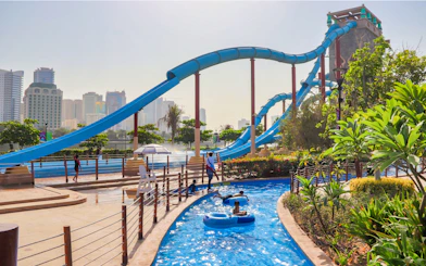 Water slides and lazy river at Al Montazah Water Park, Sharjah, with city skyline in background.