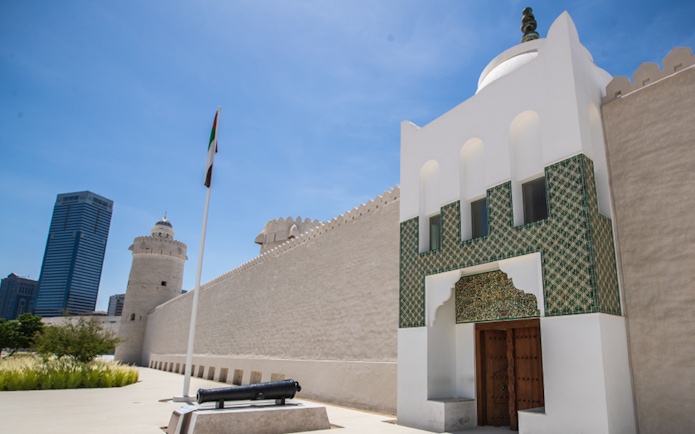 Qasr Al Hosn fort entrance with UAE flag and modern skyscraper in Abu Dhabi.