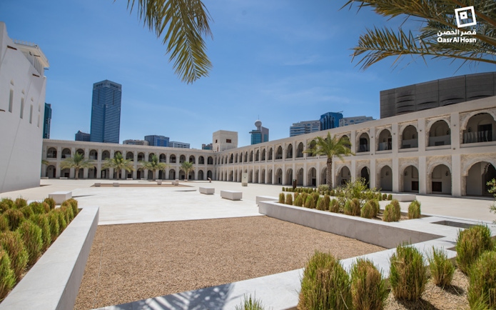 Qasr Al Hosn courtyard with palm trees and modern city skyline in Abu Dhabi.