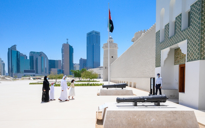 Qasr Al Hosn exterior with visitors and historic cannons, Abu Dhabi skyline in background.