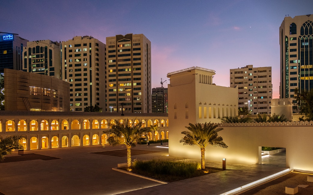 Qasr Al Hosn illuminated at dusk with modern buildings in Abu Dhabi background.
