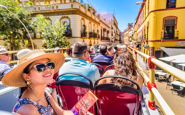 Tourists enjoying a City Sightseeing bus tour in Seville, passing historic buildings.