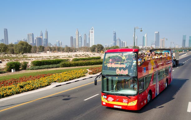 Dubai sightseeing bus with tourists, city skyline in background.
