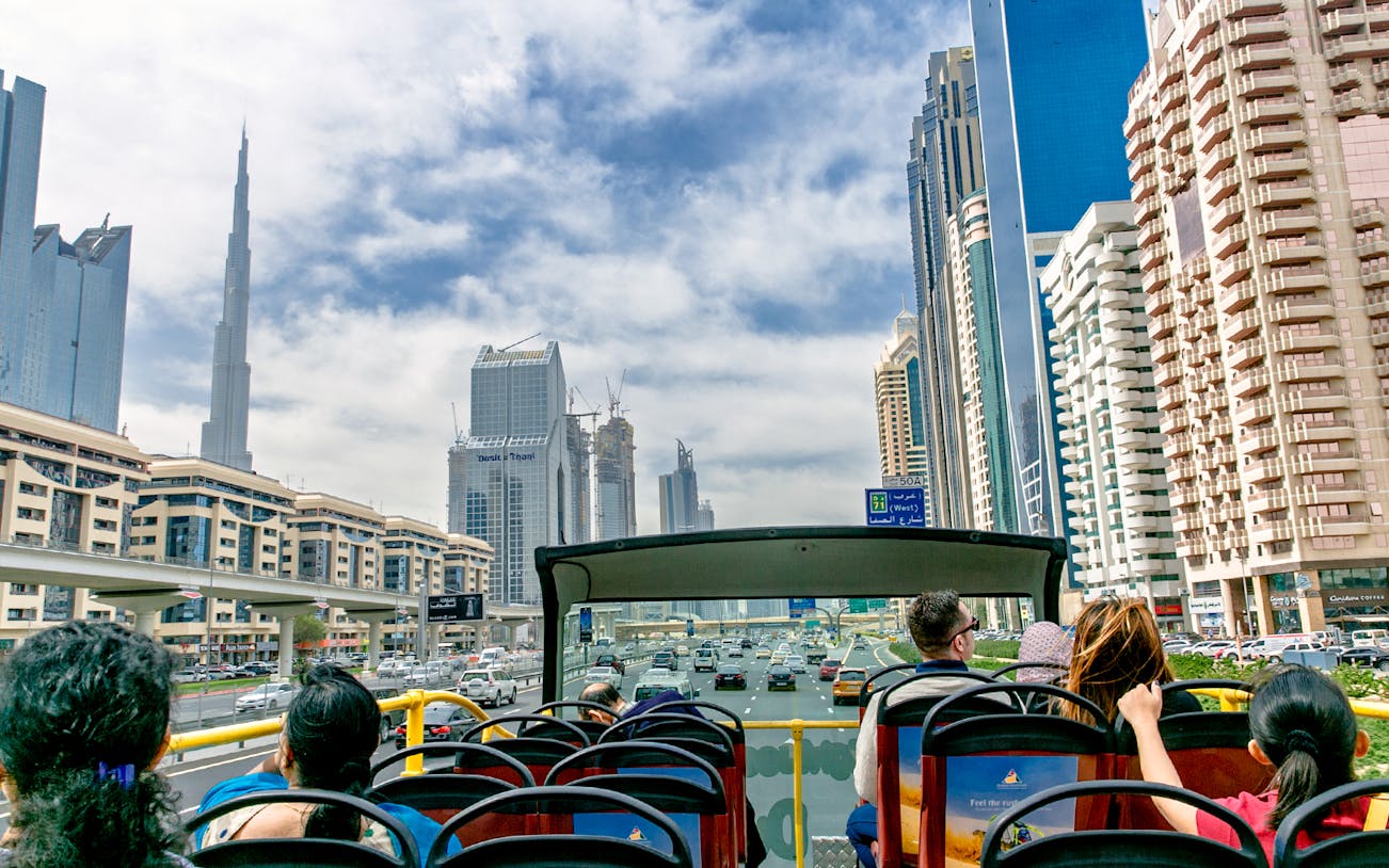 Open-top bus tour with passengers viewing Dubai skyline, including Burj Khalifa.