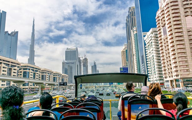 Open-top bus tour with passengers viewing Dubai skyline, including Burj Khalifa.