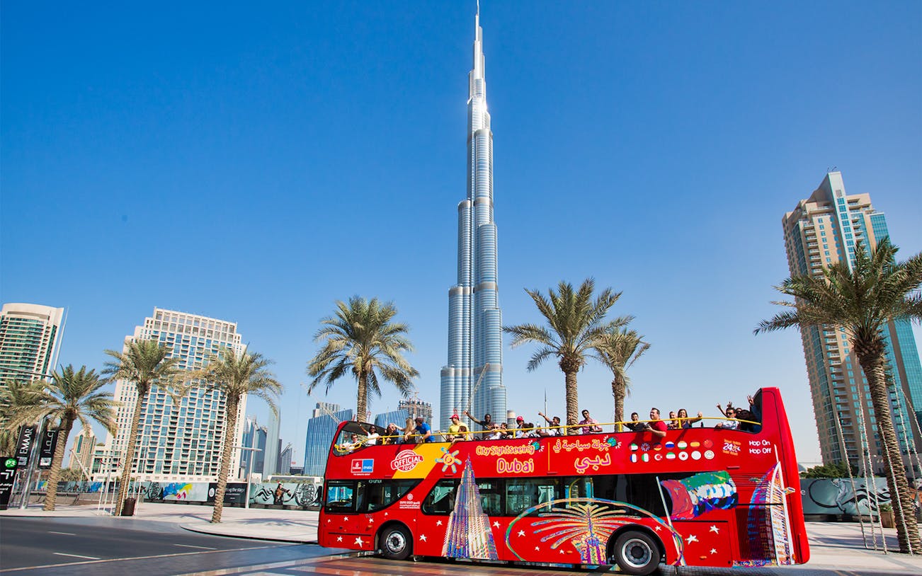 Open-top tour bus near Burj Khalifa, Dubai, with tourists enjoying the view.
