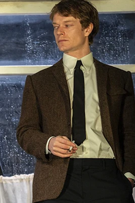 Actor in a scene from the play Hangmen, standing in front of a window with letters visible.
