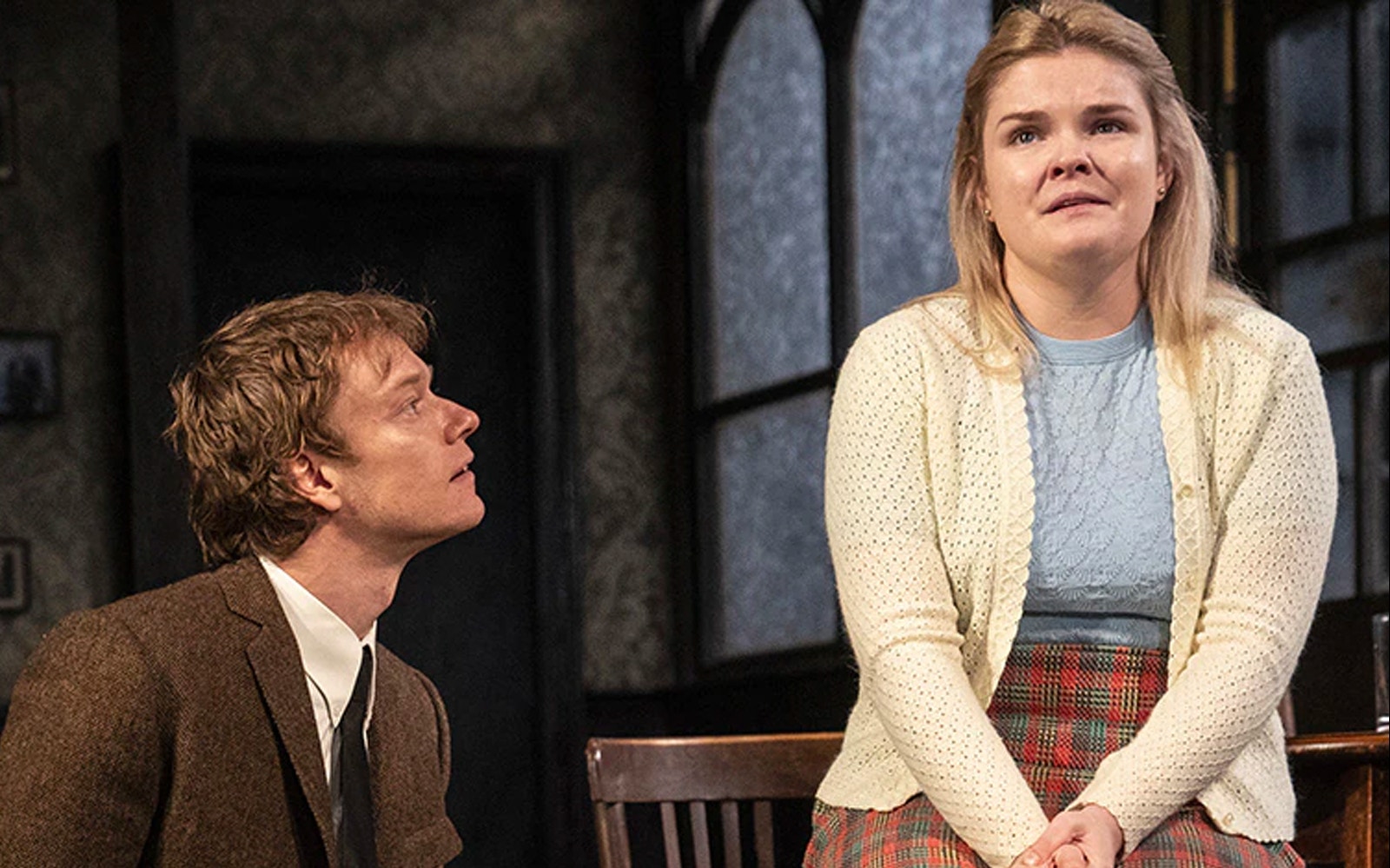 Two actors performing a scene from the play "Hangmen" in a dimly lit room.