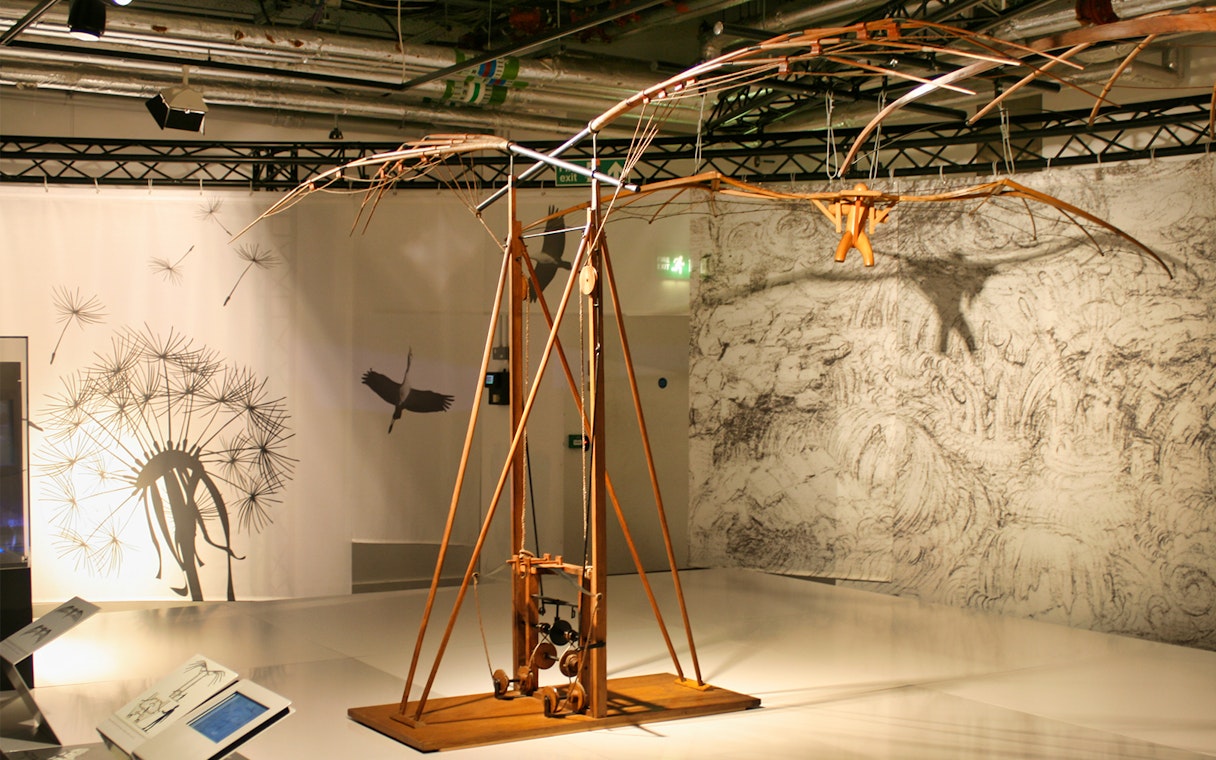 Leonardo Da Vinci Museum exhibit featuring a flying machine model with detailed sketches in the background.