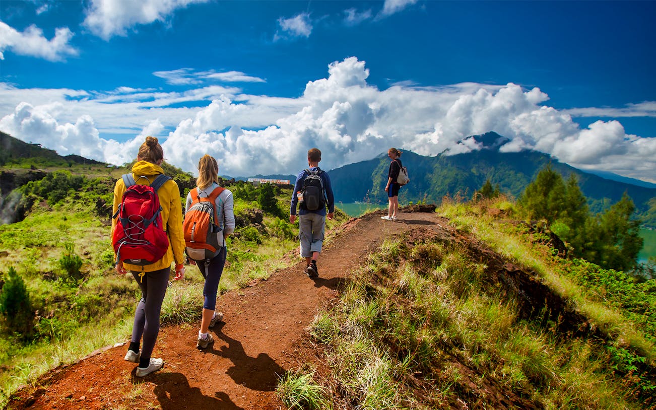 Hikers on Mount Batur trail with scenic view of mountains and clouds in Bali.