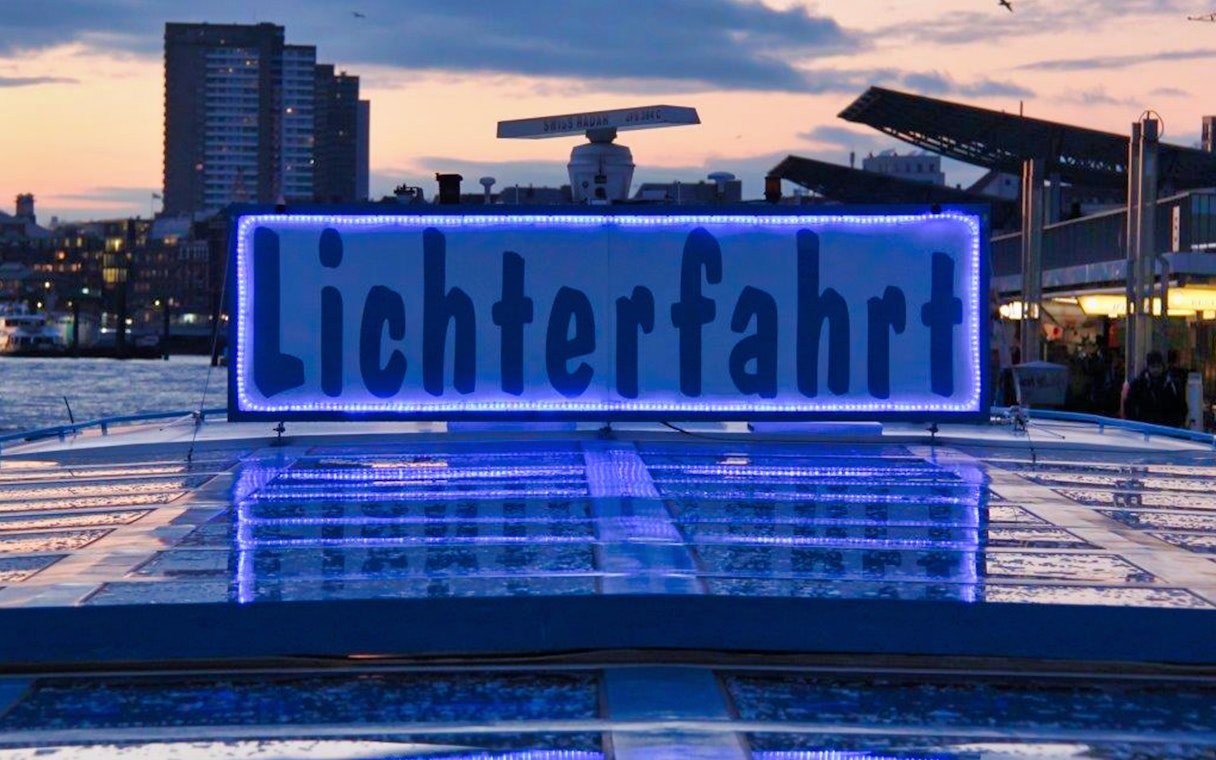 Hamburg Harbour evening cruise with illuminated "Lichterfahrt" sign on boat.