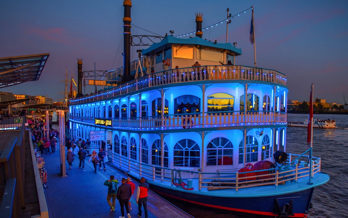Hamburg Harbour evening cruise ship illuminated with blue lights docked at the pier.