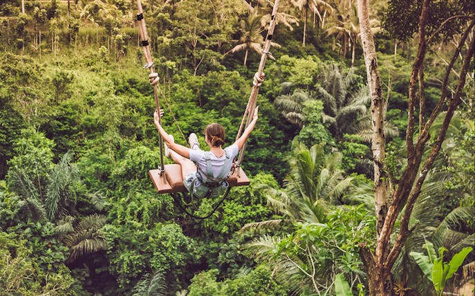 Person on a swing over lush jungle in Bali.