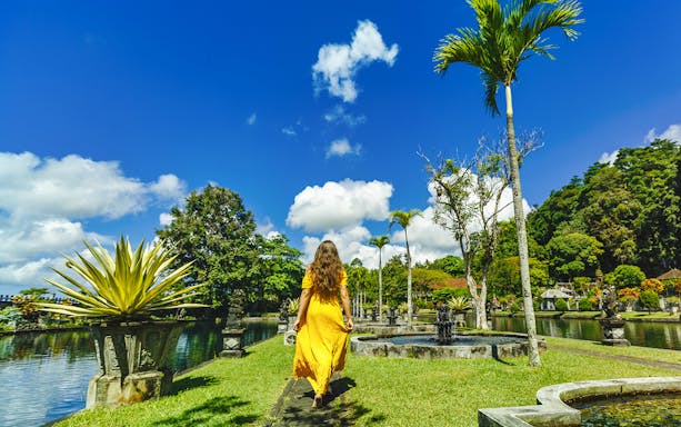 Woman walking through Tirta Gangga Water Palace gardens in Bali.