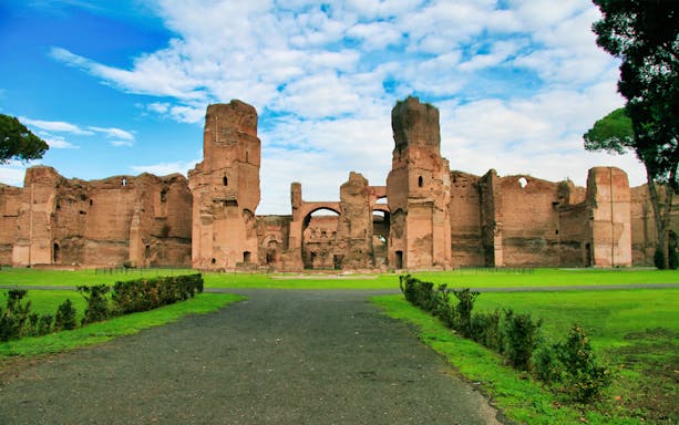 Caracalla Baths ruins in Rome with green lawns and blue sky.