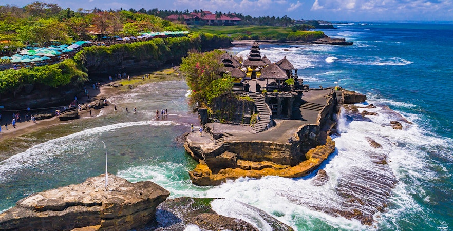 Tanah Lot Temple on a rocky outcrop surrounded by ocean waves in Bali, Indonesia.