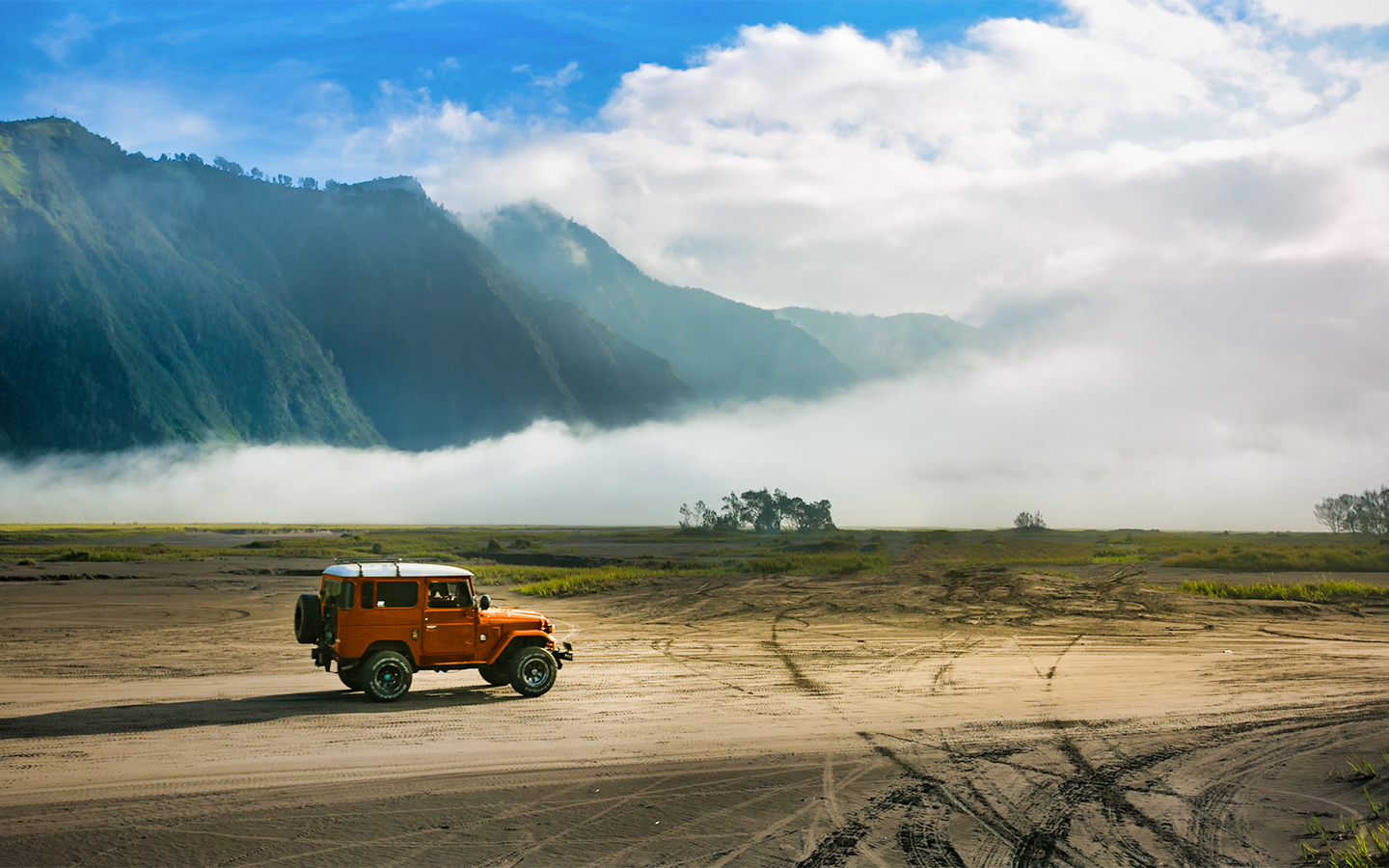 Orange jeep on sandy terrain with misty mountains in Bali.