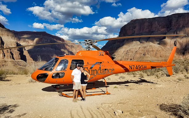 Helicopter landed on Grand Canyon floor with two people standing beside it.