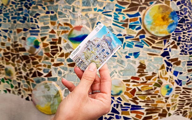 Casa Batlló ticket held in front of colorful mosaic wall in Barcelona.