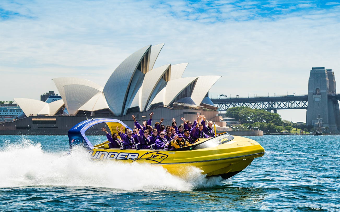 Jet boat with passengers near Sydney Opera House and Harbour Bridge.